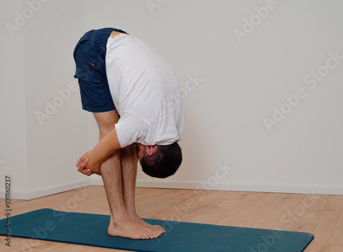 White Latino male performing open pincer pose (Uttanasana) in a yoga session at home.