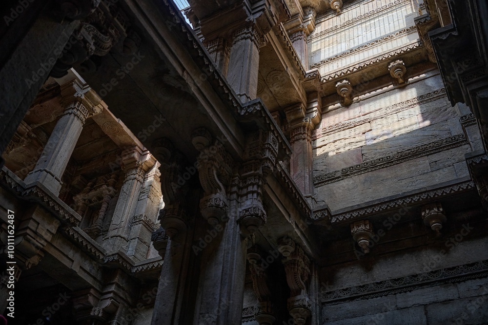 The interplay of light and shadow accentuates the carved stone pillars and intricate architectural details of the stepwell's upper levels.