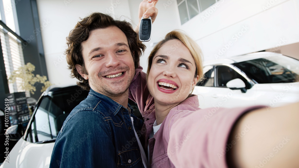 A young family is happy about buying a brand new car at a modern car dealership. A married couple takes a photo near their new car. A young family is happy about buying a brand new car at a modern car dealership. A married couple takes a photo near their new car.