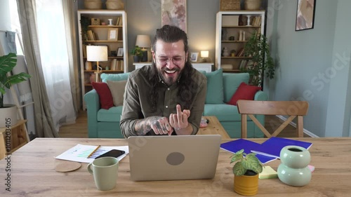 Young businessman working at home having video call with his boss giving quit on his job by showing middle finger to his employer. Funny way to quit from work after gaslight and mental burnout. photo