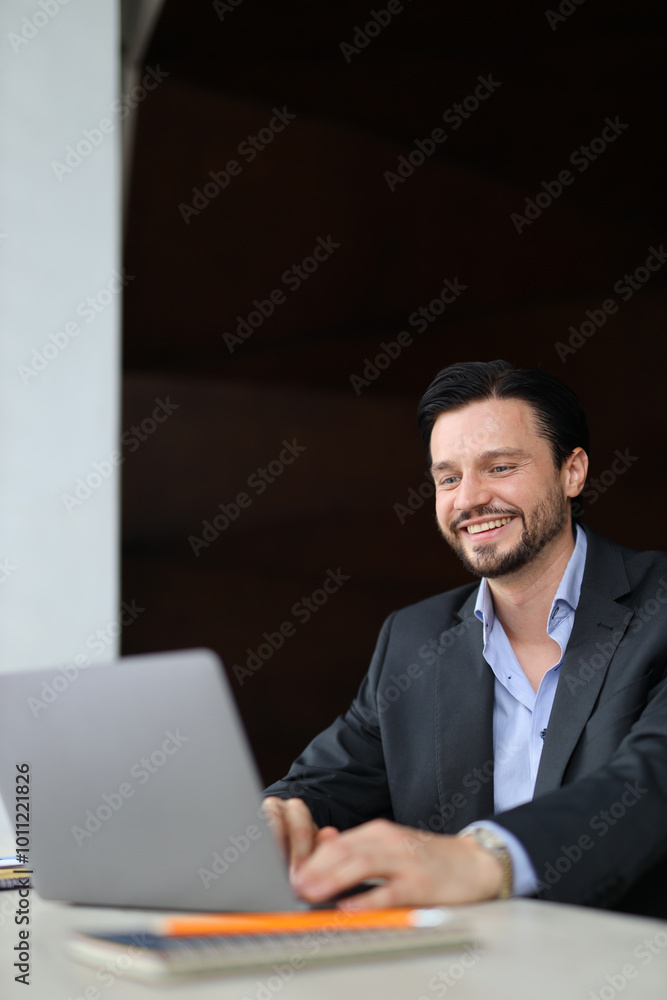 A man is sitting at a desk with a laptop in front of him. He is smiling and he is enjoying himself A man is sitting at a desk with a laptop in front of him. He is smiling and he is enjoying himself