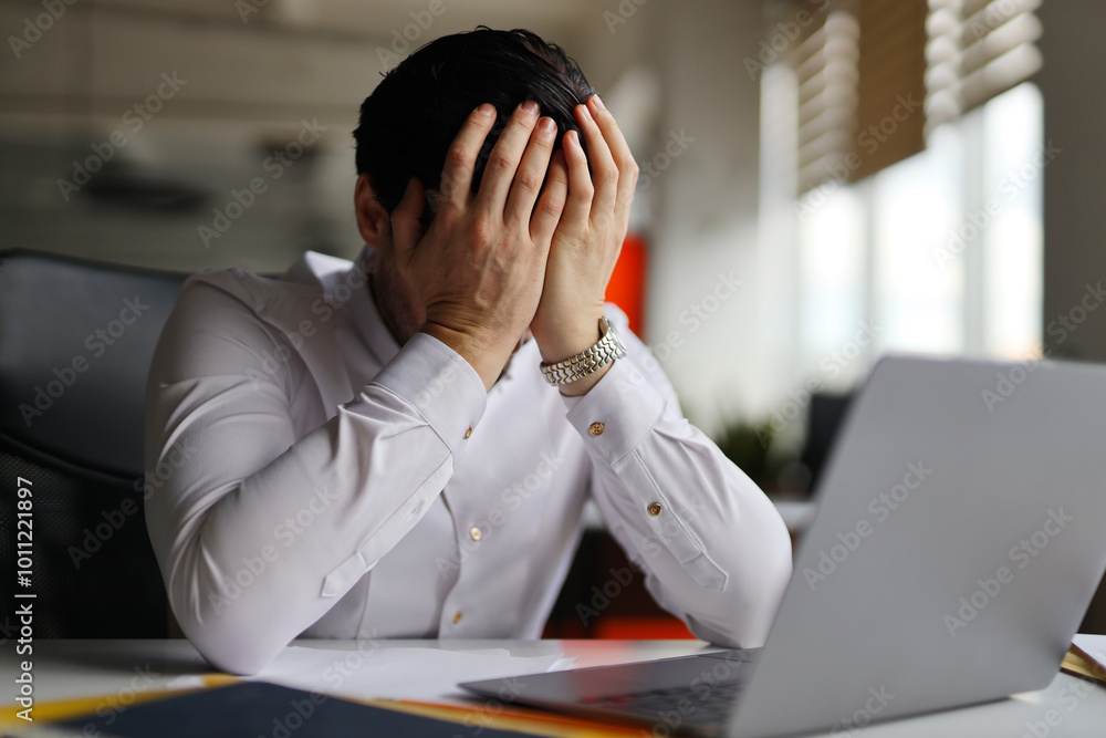 A man is sitting at a desk with a laptop and a stack of papers. He is crying and he is in distress A man is sitting at a desk with a laptop and a stack of papers. He is crying and he is in distress