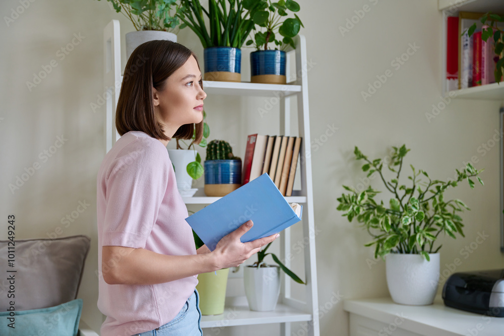 Happy smiling focused young woman reading book at home near window