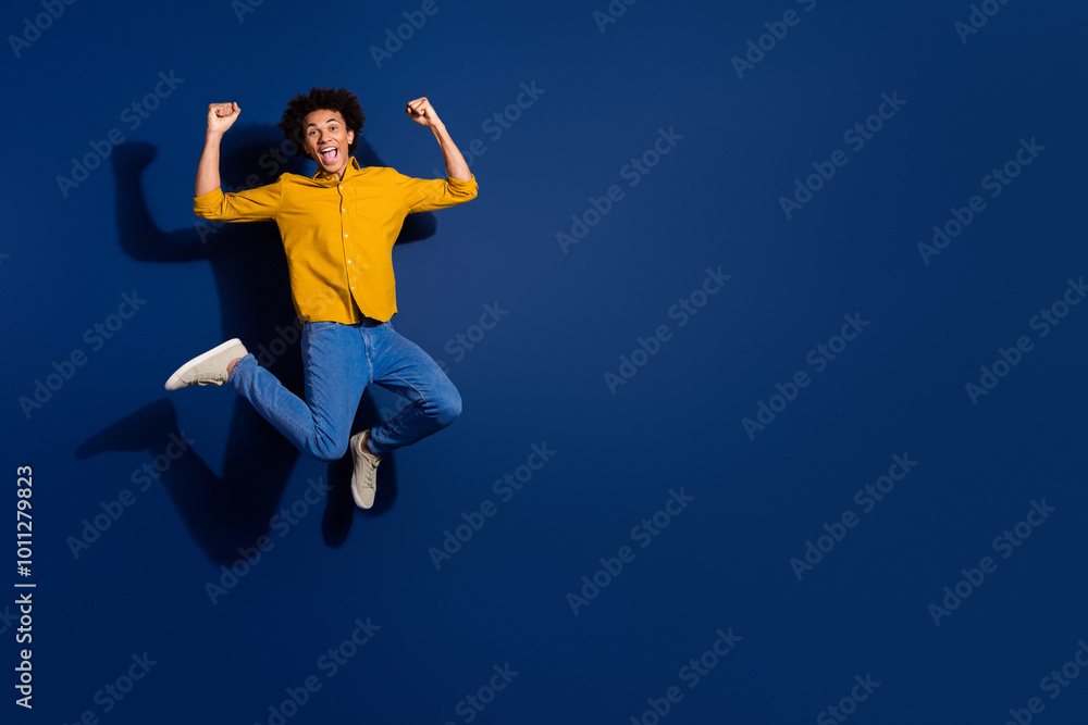 Full size photo of nice young man jump raise fists isolated on dark blue color background Full size photo of nice young man jump raise fists isolated on dark blue color background