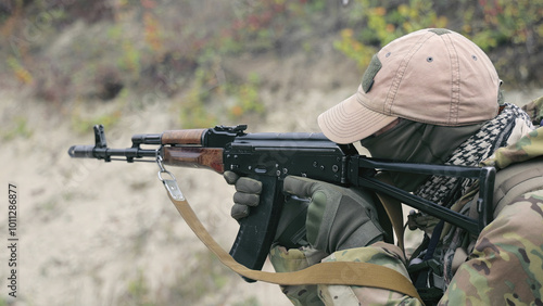 Soldier Aiming Rifle During Training. A soldier in camouflage gear and a tan cap aims a rifle during a training exercise. photo