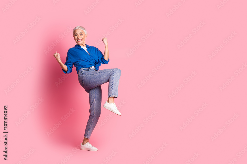 Full length photo of cheerful lucky lady dressed blue shirt smiling rising fists empty space isolated pink color background Full length photo of cheerful lucky lady dressed blue shirt smiling rising fists empty space isolated pink color background