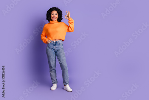 Full length photo of charming positive woman wear orange sweater showing okey empty space isolated violet color background