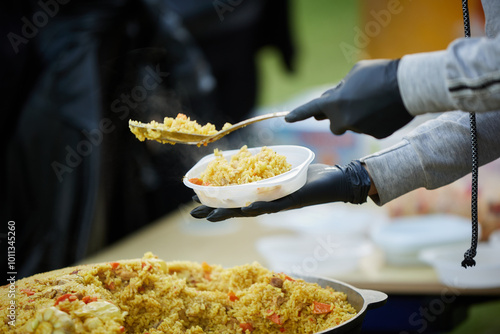 The cook pours pilaf from the cauldron into plastic plates and distributes them to people.