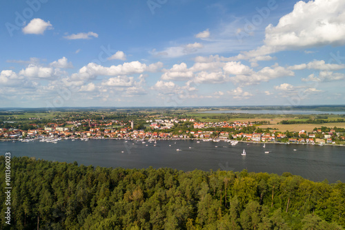 A beautiful aerial view of Mikolajki, showcasing the lush green forests, serene lake, and charming town under a blue sky with scattered clouds.