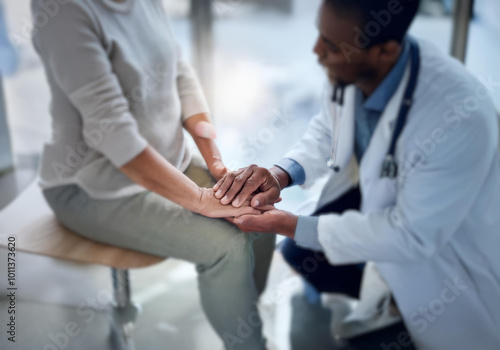 A doctor in a white coat holds the hand of a patient sitting on a chair.