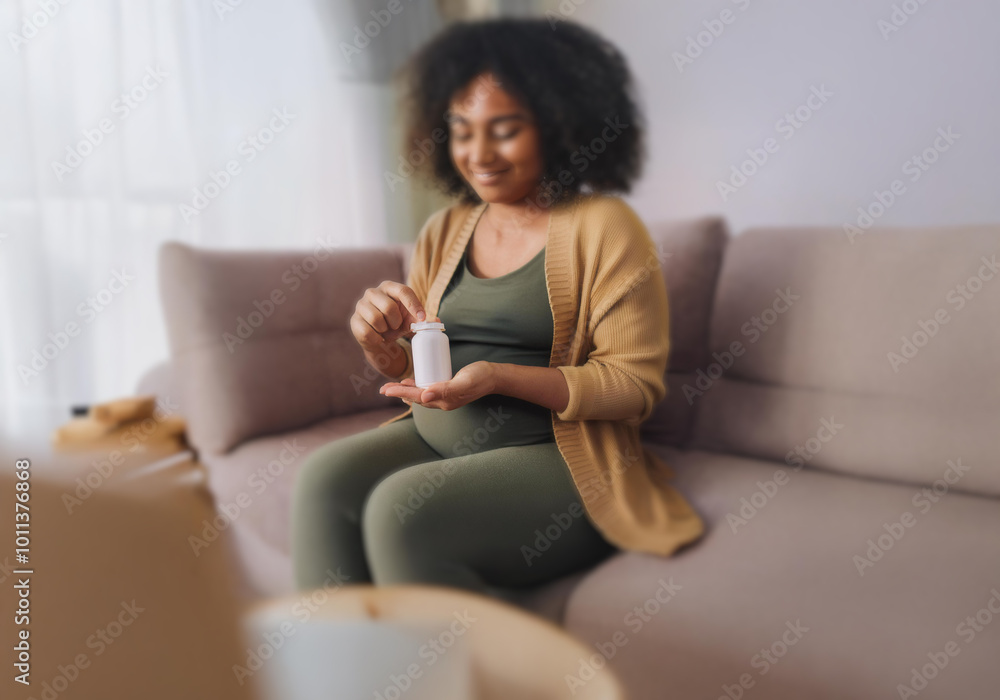A pregnant woman sits on a couch, smiling as she holds a white bottle in her hand. A pregnant woman sits on a couch, smiling as she holds a white bottle in her hand.