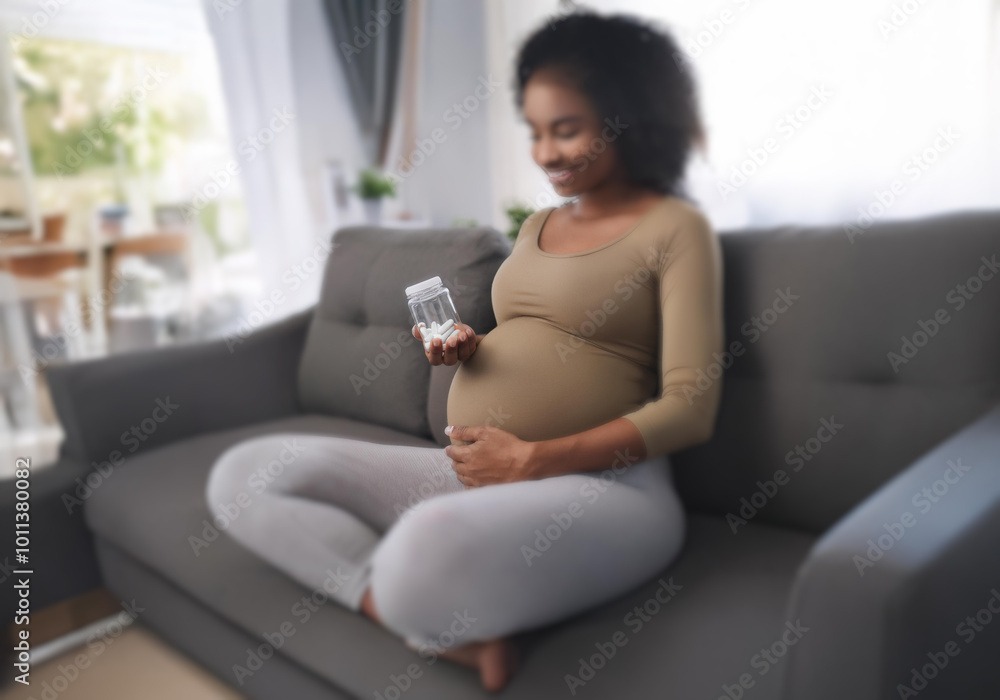 A pregnant woman sits on a couch holding a bottle of pills. A pregnant woman sits on a couch holding a bottle of pills.