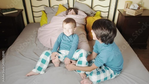 Two children tickle the feet of their brother who is rolled up in a duvet.