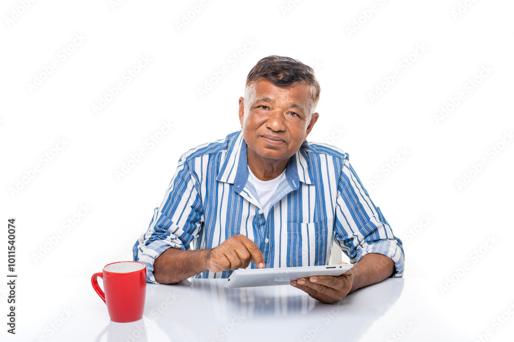 Happy elderly Asian man using teblet PC computer with red cup at desk isolated on white background. Happy elderly Asian man using teblet PC computer with red cup at desk isolated on white background.