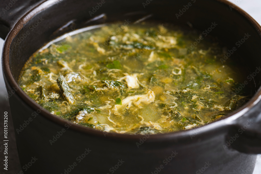 Soup with green sorrel in black ceramic pot on gray background Soup with green sorrel in black ceramic pot on gray background
