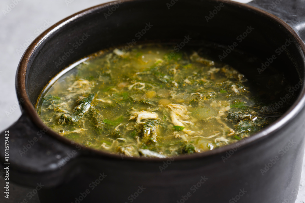 Soup with green sorrel in black ceramic pot on gray background Soup with green sorrel in black ceramic pot on gray background