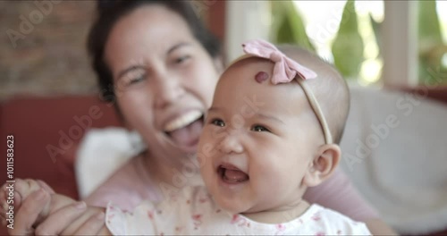 Portrait – cute happy Asian baby girl laughing and showing gummy smile while playing with mom at home. Looking at camera shot.