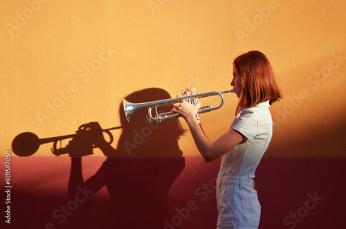 A young girl is playing a trumpet in front of orangewall.  photo