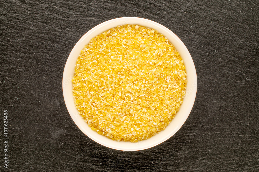 Uncooked corn grits with ceramic cup on slate stone, macro, top view. Uncooked corn grits with ceramic cup on slate stone, macro, top view.