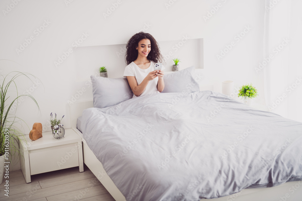 Full size photo of young adorable lady lying bed hold device dressed sleepwear chill apartment waking up hotel bedroom white light interior Full size photo of young adorable lady lying bed hold device dressed sleepwear chill apartment waking up hotel bedroom white light interior