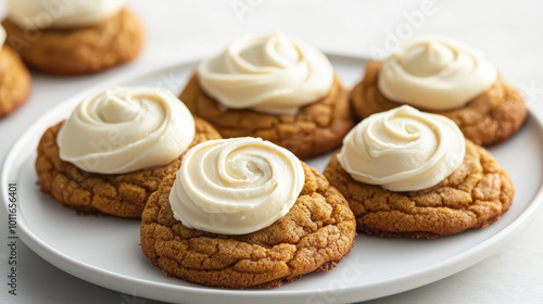 Freshly baked frosted cookies arranged on a white plate, showcasing creamy swirls of frosting on a warm, golden-brown base