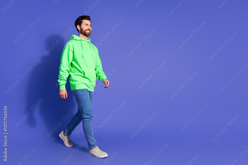 Full body photo of attractive young man walking empty space dressed stylish green clothes isolated on violet color background Full body photo of attractive young man walking empty space dressed stylish green clothes isolated on violet color background
