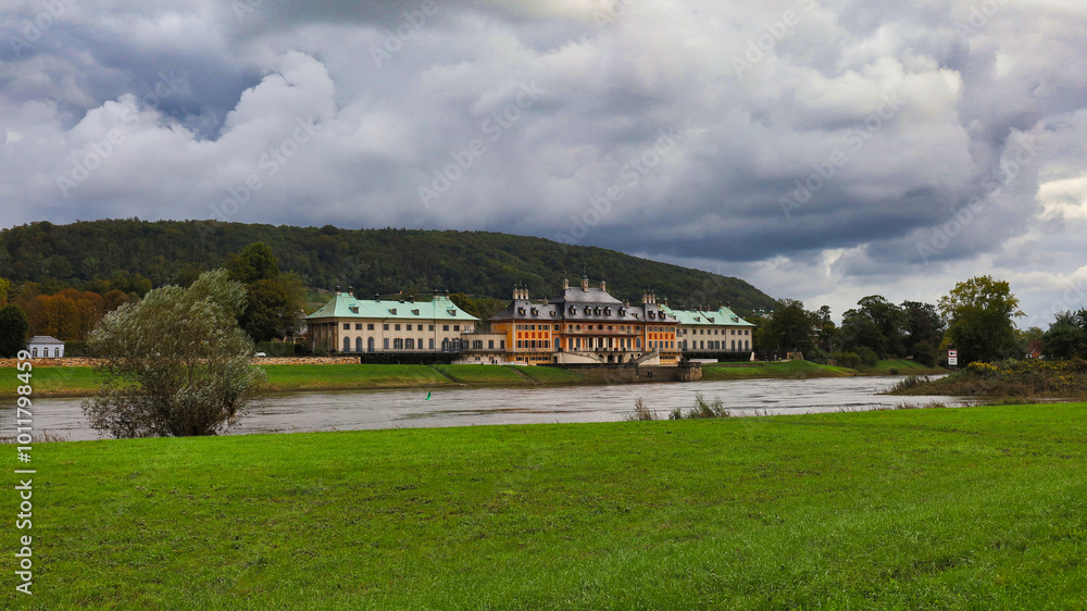 Obraz premium Weitwinkel-Ansicht von Schloss Pillnitz mit den Elbwiesen im Vordergrund unter einem imposanten Wolkenhimmel im herbstlichen Dresden, Sachsen, Deutschland