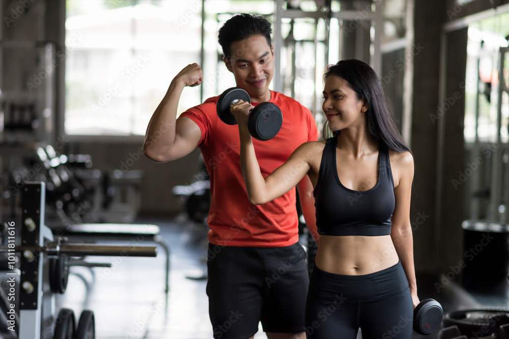Fototapeta premium Young Asian woman raise dumbbell with boyfriend in gym