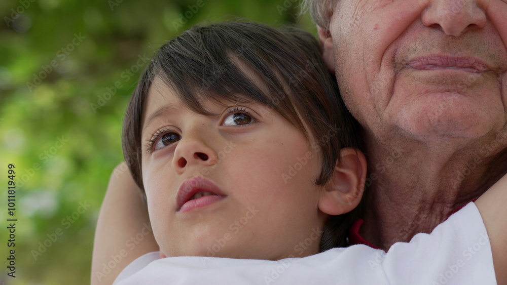 Close-up of grandfather and grandson embracing, both looking thoughtful and content, with a background of green foliage, capturing a tender moment of family love and connection Close-up of grandfather and grandson embracing, both looking thoughtful and content, with a background of green foliage, capturing a tender moment of family love and connection