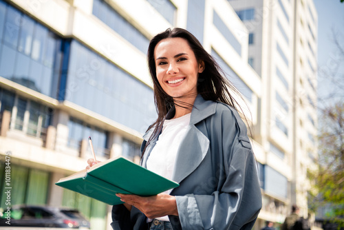 Photo of cheerful pretty lady dressed grey jacket writing story enjoying sunshine outdoors town street