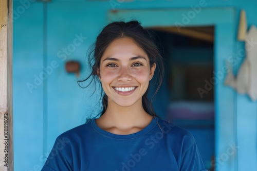 Portrait of a young woman with a bright smile, wearing a blue shirt, standing in a rural setting