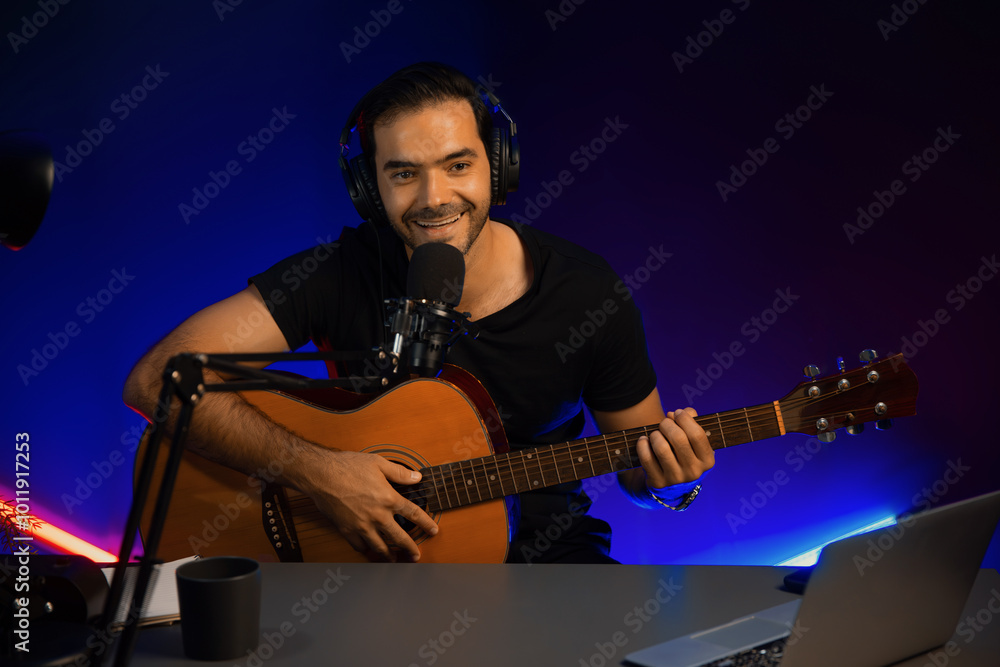 Host channel of smart influencer in creative audio on live streaming to fanclub with sing with play guitar music blogger using headset and mic social media online at neon light modern studio. Surmise. Host channel of smart influencer in creative audio on live streaming to fanclub with sing with play guitar music blogger using headset and mic social media online at neon light modern studio. Surmise.