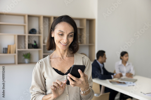 Happy middle aged Hispanic woman multiethnic business team member enjoy receiving good news by phone. Elderly businesswoman distracted from office work fell glad to help answer client via social media