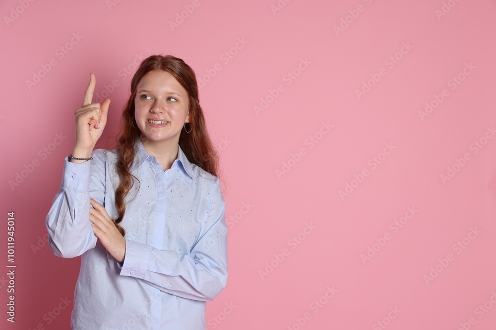 Happy teenage girl pointing upwards on pink background. Space for text Happy teenage girl pointing upwards on pink background. Space for text