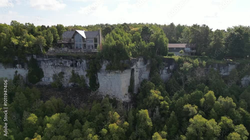 Drone view pulling away from a cliff with lush tree canopies and a house on top of a cliff Drone view pulling away from a cliff with lush tree canopies and a house on top of a cliff