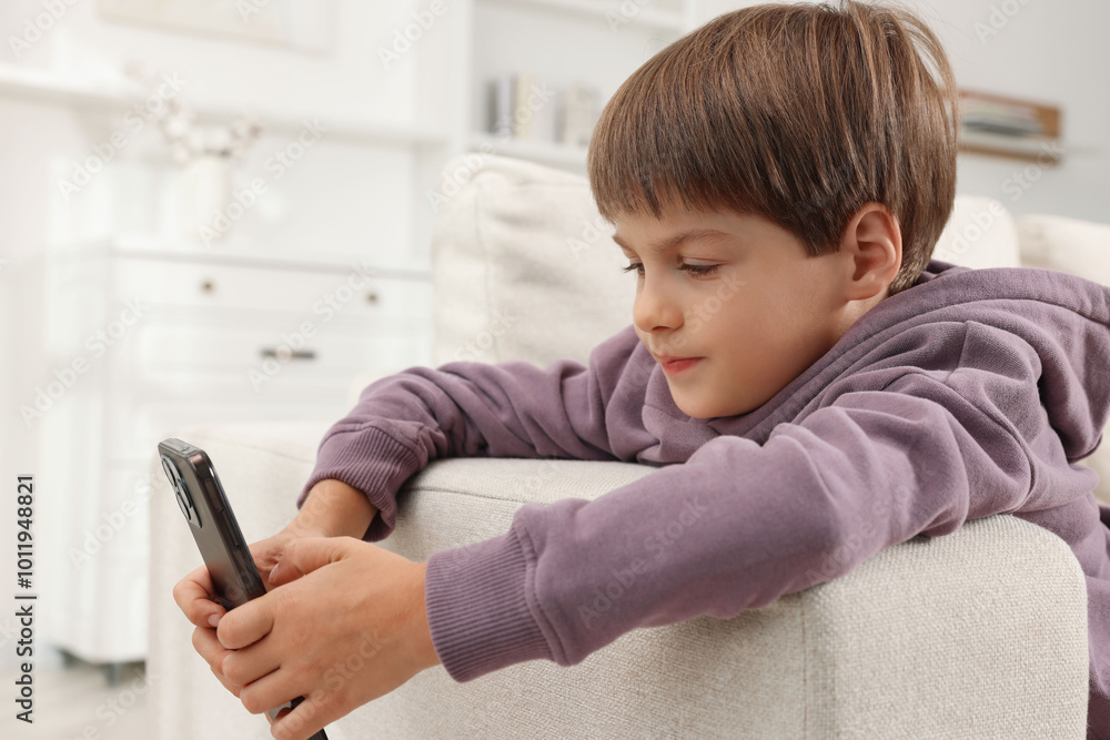 Cute little boy using smartphone on sofa at home Cute little boy using smartphone on sofa at home