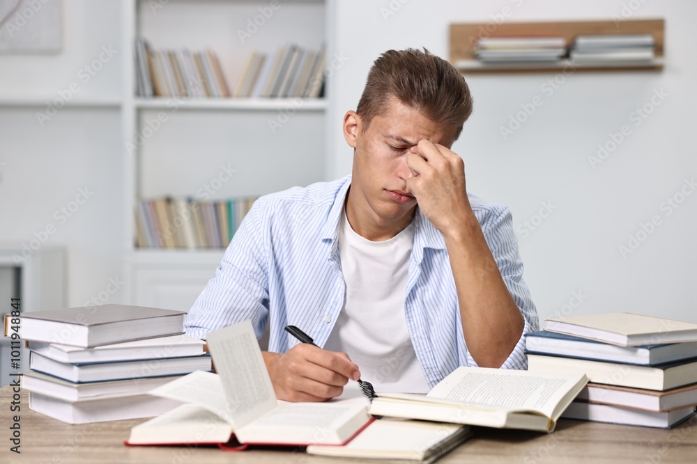 Tired student before exam at table among books indoors Tired student before exam at table among books indoors