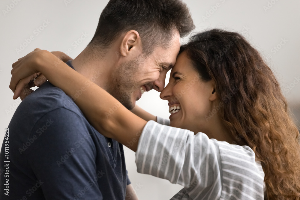 Cheerful attractive couple in love hugging with faces touch, talking, laughing, dancing together at home, enjoying romance, celebrating Valentines day, marriage anniversary. Side view portrait Cheerful attractive couple in love hugging with faces touch, talking, laughing, dancing together at home, enjoying romance, celebrating Valentines day, marriage anniversary. Side view portrait
