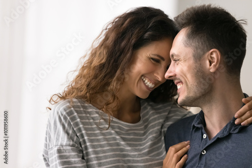 Cheerful young married couple in love enjoying happiness, romance, closeness, laughing, talking, having fun in close family relationship. Pretty Latin wife hugging husband with faces touch