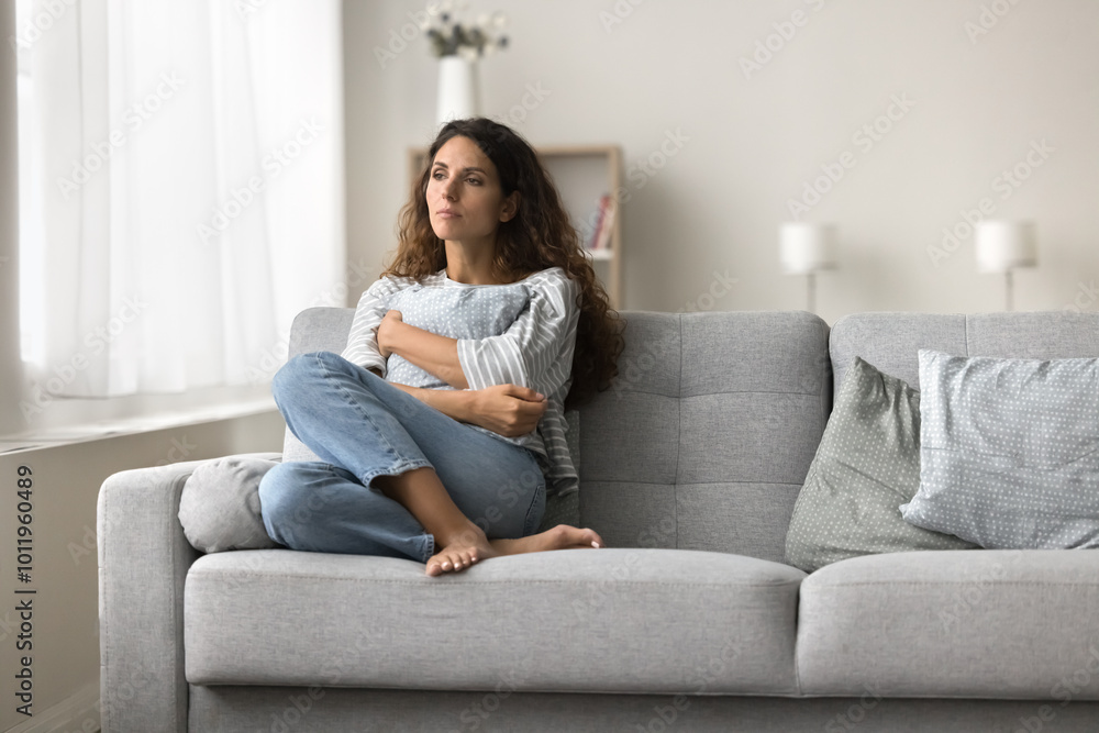 Sad lonely young woman sitting on couch in modern home interior, keeping closed pose, tightening pillow, suffering from depression, apathy after stress, trauma, loss Sad lonely young woman sitting on couch in modern home interior, keeping closed pose, tightening pillow, suffering from depression, apathy after stress, trauma, loss