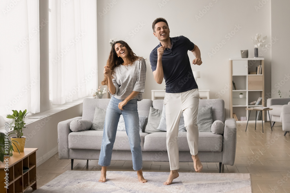 Cheerful active young couple enjoying active leisure, entertainment at home, dancing disco in spacious new living room, smiling, laughing, celebrating anniversary Cheerful active young couple enjoying active leisure, entertainment at home, dancing disco in spacious new living room, smiling, laughing, celebrating anniversary