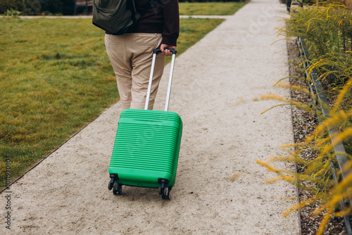 Obraz na płótnie Unrecognizable man pulling green suitcase outdoors. Rear view. Copy space. Man walking on the street with travel bag. w salonie