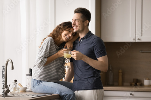 Foto Happy married couple in love hugging in kitchen, drinking hot beverages, enjoyin