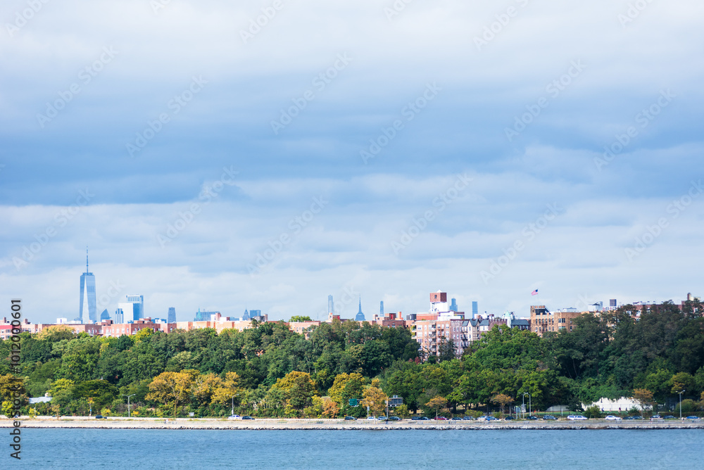 Fototapeta premium The shoreline near the Verrazzano-Narrows Bridge showcases the peaceful Bay Ridge neighborhood, where houses nestle among lush greenery, creating a serene contrast to the bustling city beyond.