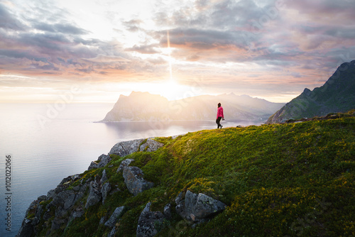 Breathtaking view of a young woman climber hiking on cliff over a stunning fjord landscape during a vibrant sunset or sunrise