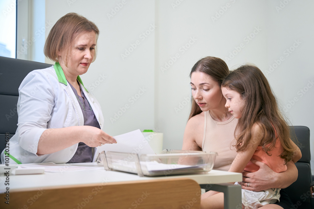 Doctor showing medical report to a mother and daughter Doctor showing medical report to a mother and daughter