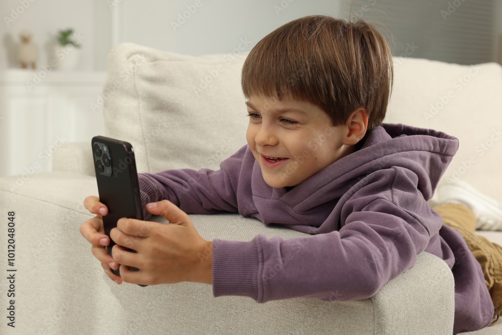 Cute little boy using smartphone on sofa at home Cute little boy using smartphone on sofa at home