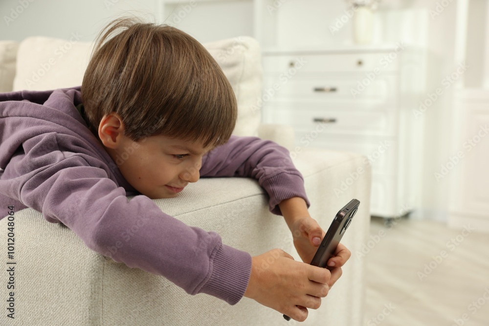 Cute little boy using smartphone on sofa at home Cute little boy using smartphone on sofa at home