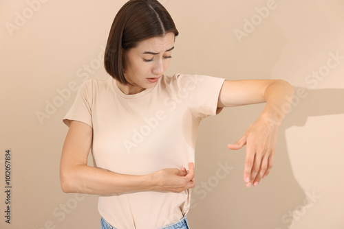 Emotional woman in t-shirt before using deodorant on beige background