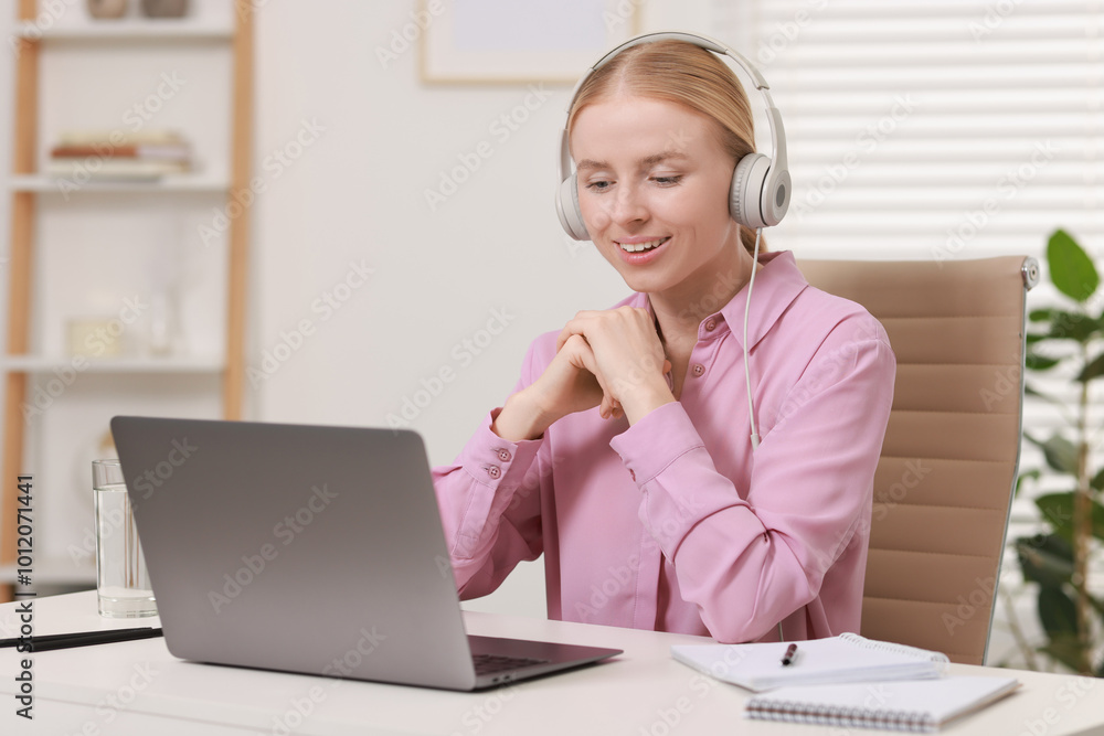 Interpreter in headphones working with laptop at table indoors Interpreter in headphones working with laptop at table indoors